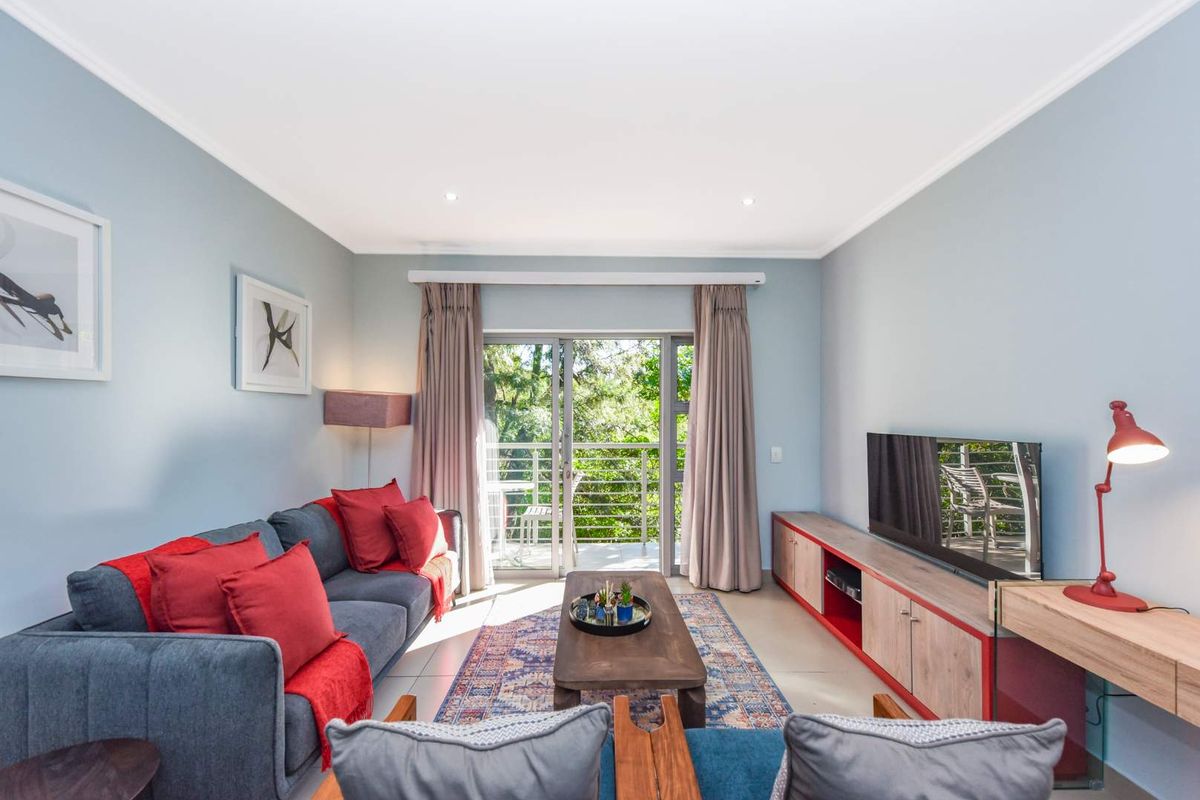 A bright and well-maintained living room featuring tiled flooring, recessed lighting, and a sliding glass door that opens onto a balcony with greenery views.