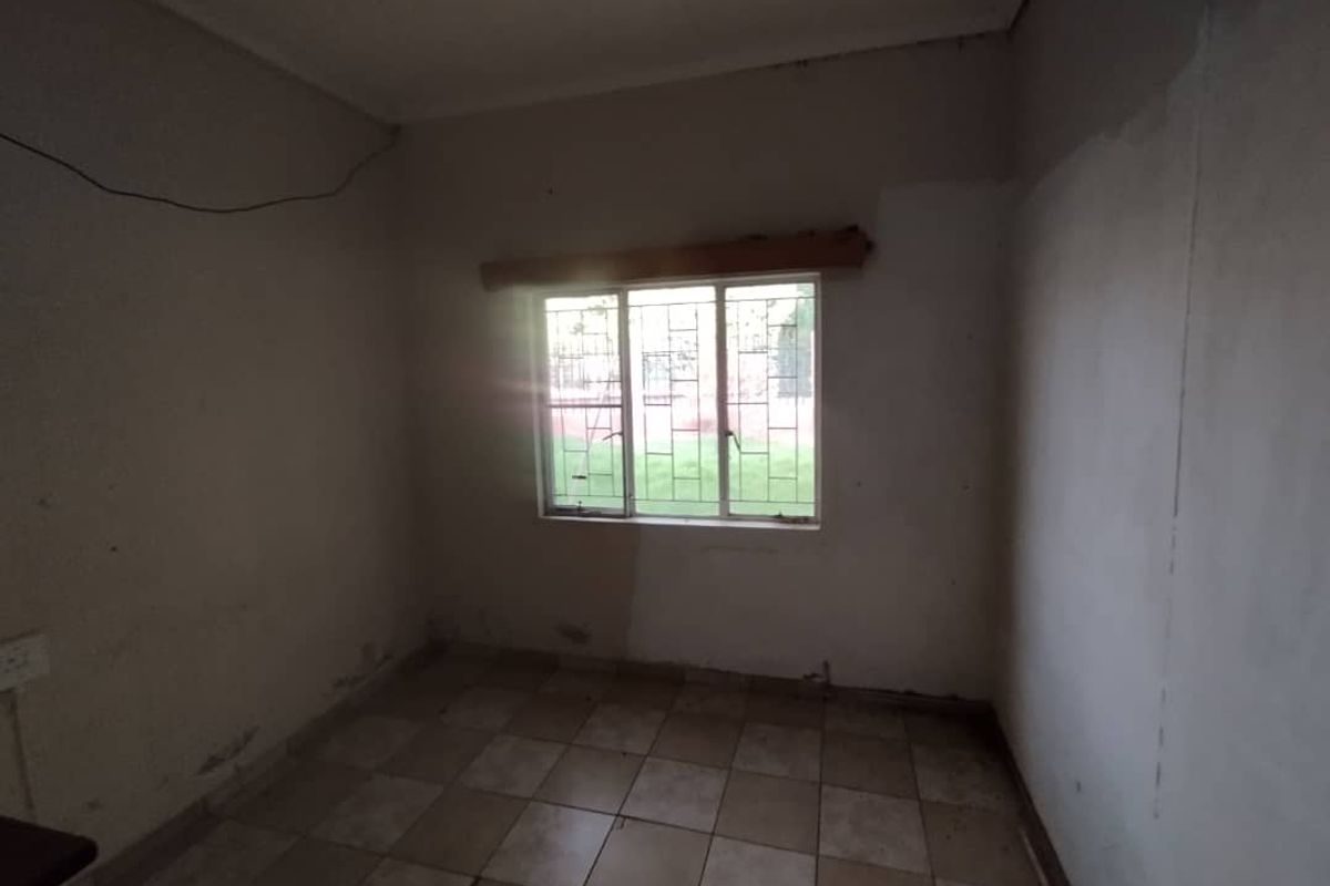 An empty bedroom featuring tiled flooring and a window with security bars, requiring cosmetic updates and wall repairs.