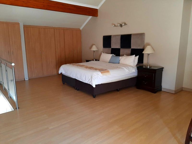 Spacious bedroom featuring laminate flooring, built-in cupboards, and an exposed timber beam, with a mezzanine-style layout overlooking the lower level.