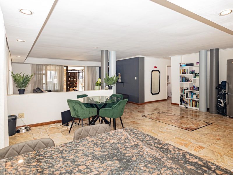 Spacious open-plan living and dining area featuring tiled flooring, recessed lighting, structural columns, and a granite-topped kitchen island.