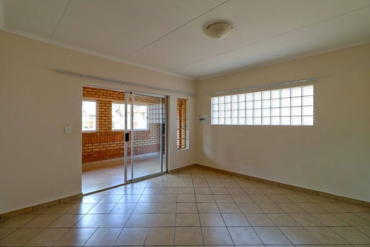 An empty living room featuring tiled flooring, a glass block window, and a sliding door leading to an enclosed patio area.
