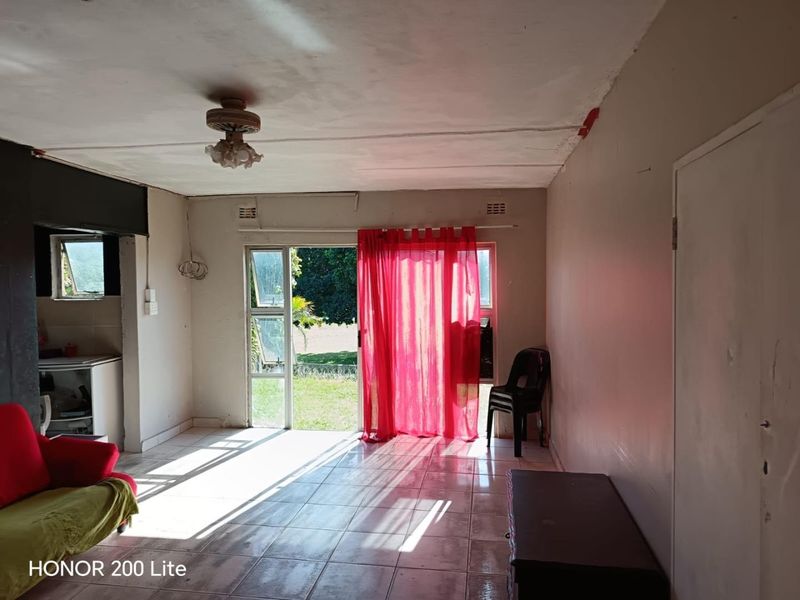 Living room with tiled flooring and sliding glass door access to the garden, featuring dated finishes and visible ceiling wear.