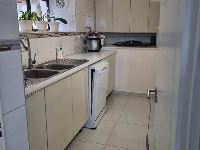 A functional kitchen featuring neutral built-in cabinetry, tiled flooring, a double bowl stainless steel sink, and a tiled backsplash.