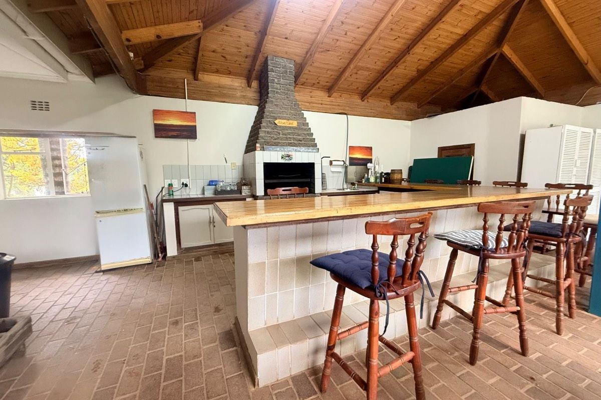 Spacious entertainment area featuring a built-in brick fireplace, wooden vaulted ceiling, and a large tiled bar counter with brick flooring.