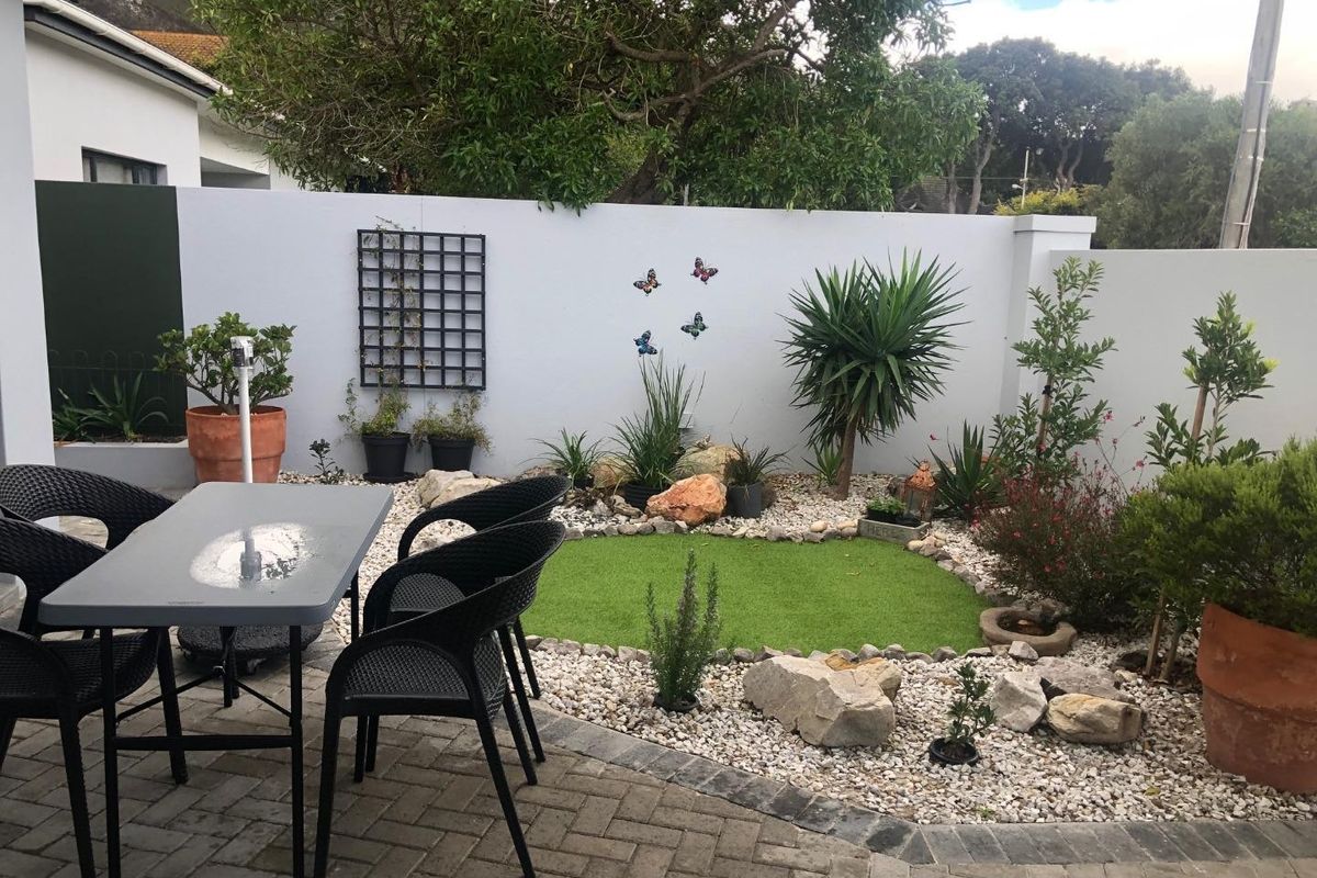 A low-maintenance rear courtyard featuring paved flooring, a small artificial grass area, decorative stone landscaping, and a perimeter boundary wall.
