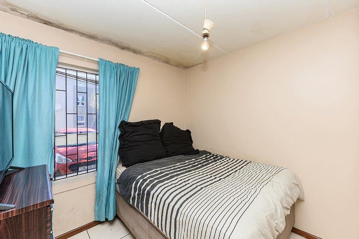 A bedroom featuring tiled flooring and security bars on the window, showing visible signs of ceiling water damage and maintenance requirements.