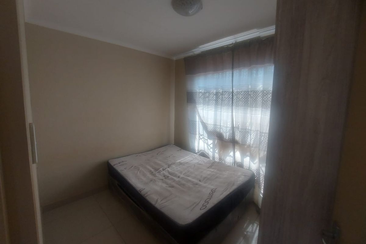 A compact bedroom featuring tiled flooring and a window with fitted curtain tracks.