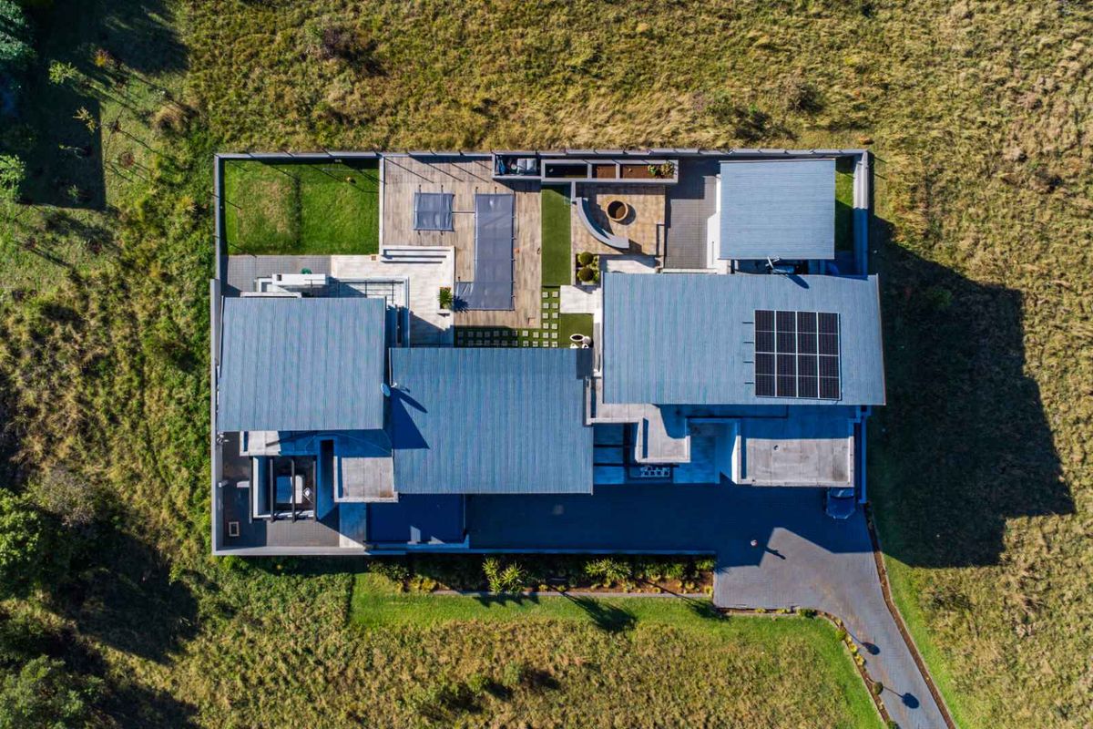 Aerial view of a modern residential property featuring a metal roof, integrated solar panels, paved driveway, and landscaped garden areas.
