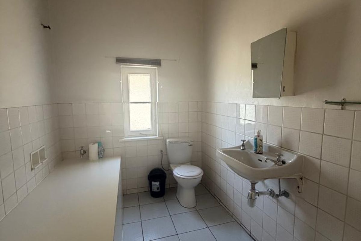 A dated bathroom featuring white wall and floor tiles, a wall-mounted basin, and a built-in vanity counter, offering potential for modernization.