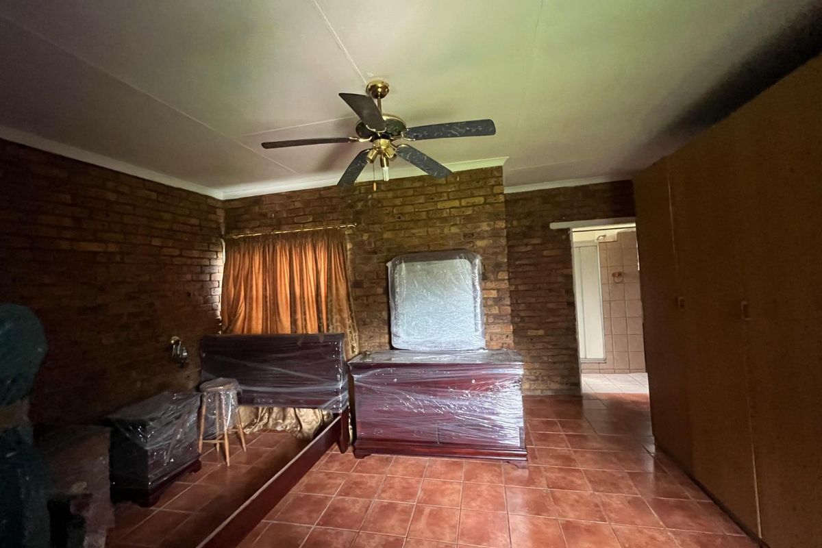 Spacious bedroom featuring exposed brick walls, tiled flooring, a ceiling fan, and an en-suite bathroom access.