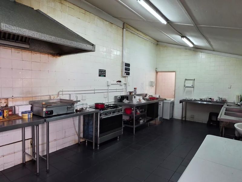 Commercial kitchen space featuring stainless steel prep surfaces, gas stove, extractor hood, double sink, and tiled finishes throughout.
