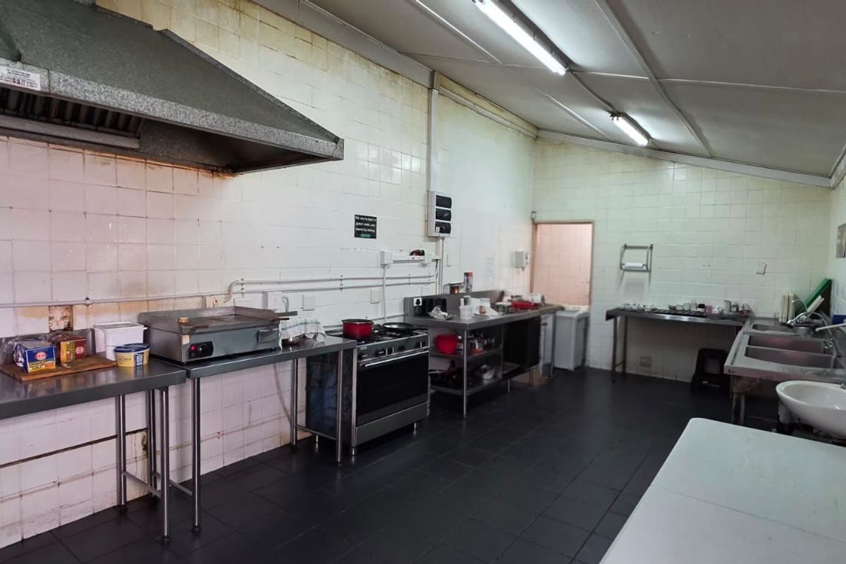 Commercial kitchen space featuring stainless steel prep surfaces, gas stove, extractor hood, double sink, and tiled finishes throughout.