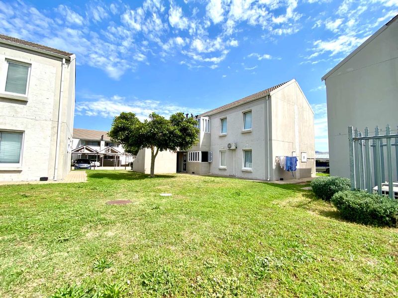 A view of the rear exterior of the apartment complex, featuring a shared lawn area, paved pathways, and building facades with mounted air conditioning units.