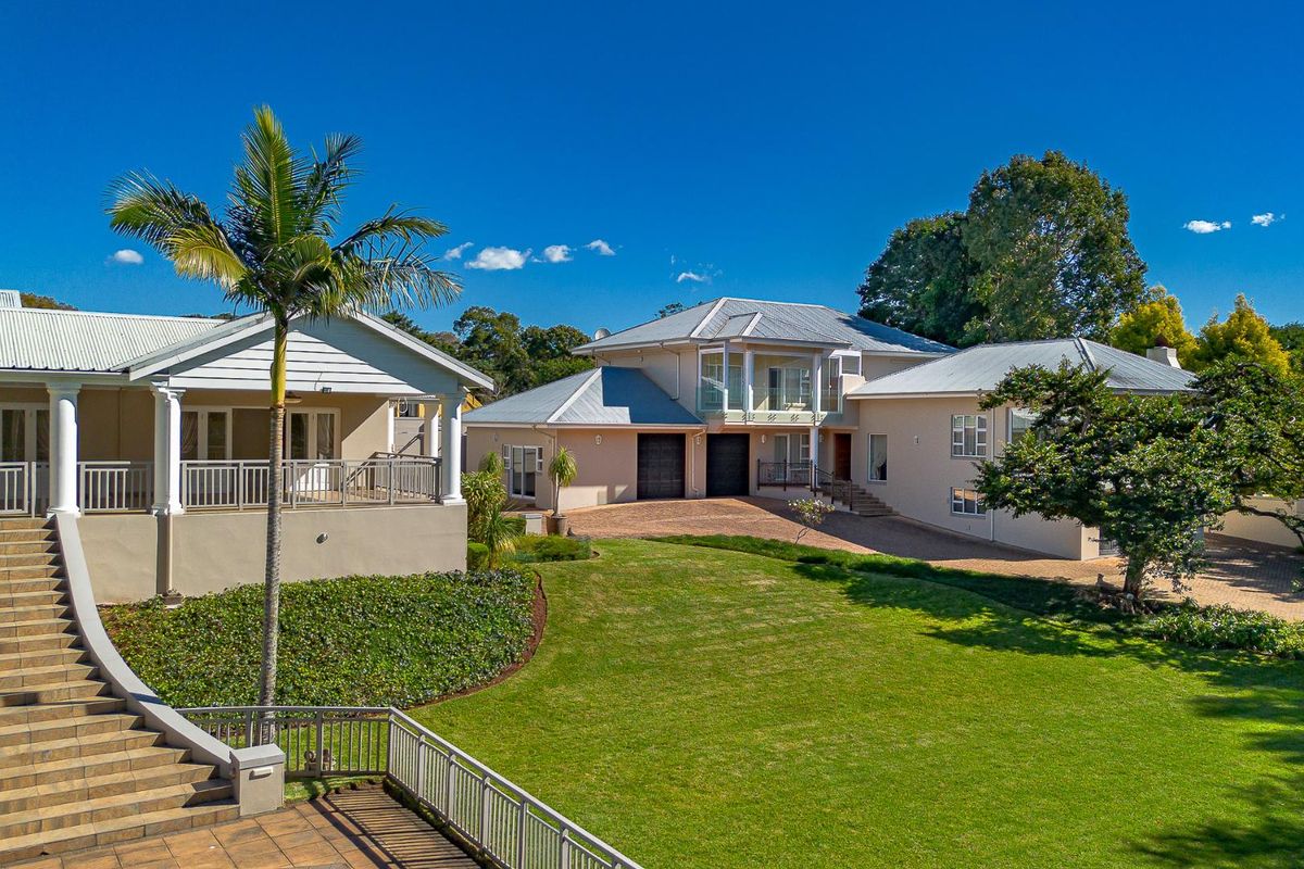 An elevated view of a large residential property featuring a well-maintained lawn, paved driveway, double garage, and multiple covered patio areas.