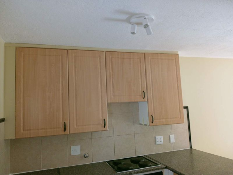 A functional kitchen area featuring light wood-finish cabinetry, a tiled backsplash, and a built-in electric hob, ready for modern updates.