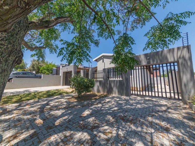 Front exterior view of the property featuring a paved driveway, secure perimeter wall with electric fencing, and a metal entrance gate.