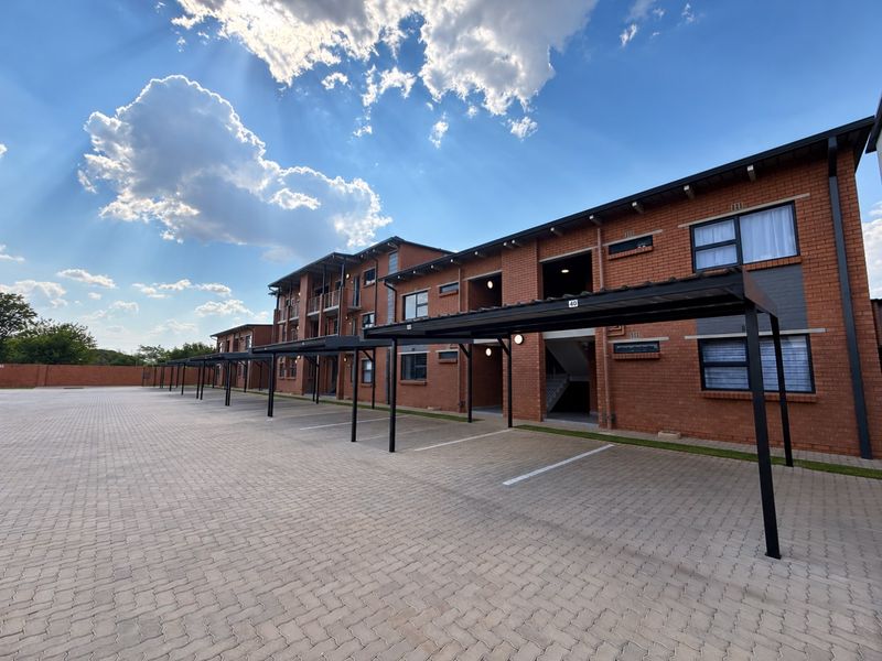 A well-maintained apartment complex exterior featuring a paved parking area with covered carports and a classic red brick facade.