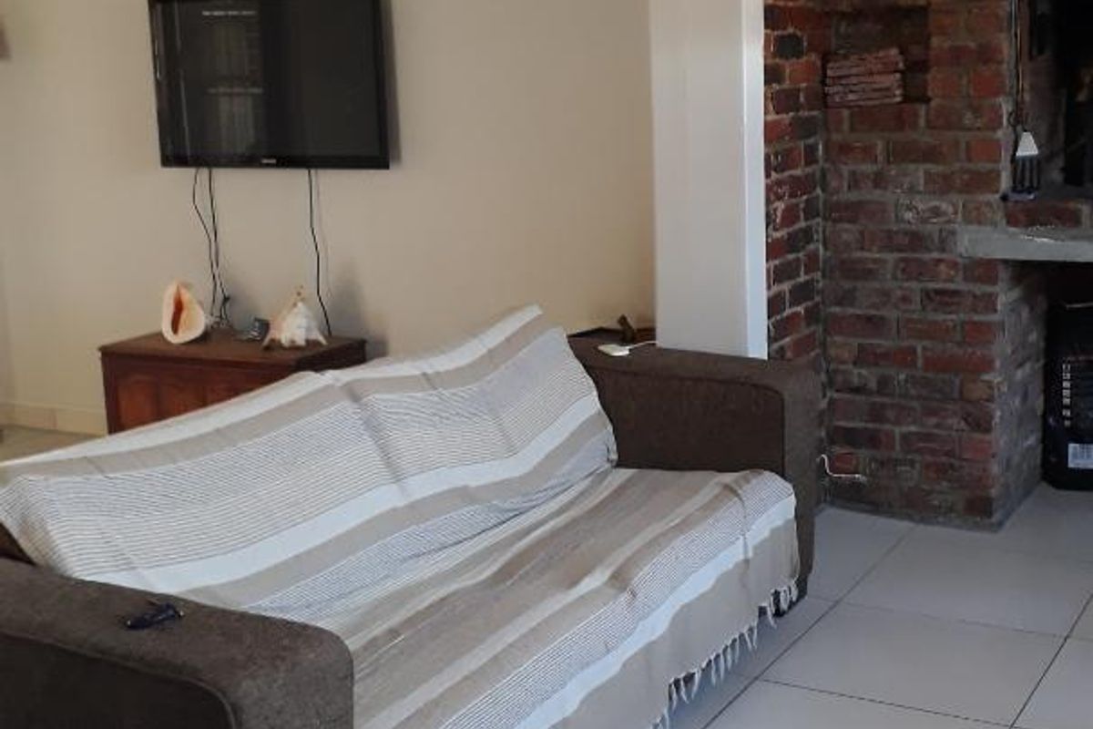A living room featuring tiled flooring and a prominent exposed brick fireplace, offering a cozy and functional space.