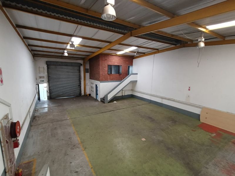 Spacious industrial warehouse unit featuring a roller shutter door, mezzanine level, exposed steel roof trusses, and durable concrete flooring.