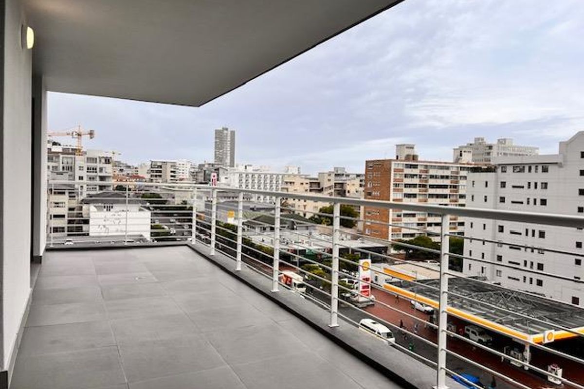 A spacious, modern balcony featuring clean tiled flooring and a secure metal balustrade, offering an elevated urban view.