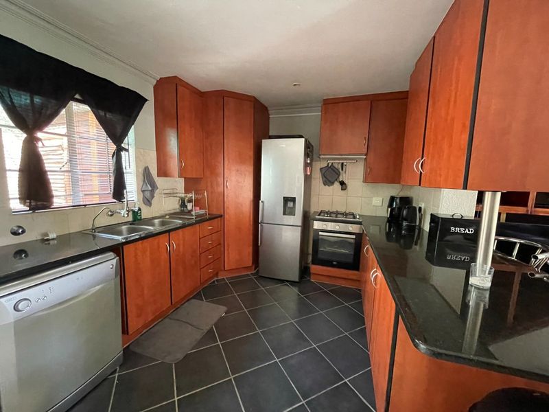 A functional kitchen featuring wooden cabinetry, granite countertops, a double basin sink, and built-in cooking appliances with dark tiled flooring.