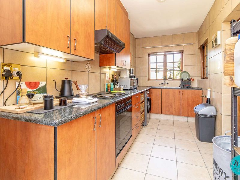 A functional kitchen featuring wood-finish cabinetry, granite countertops, a built-in oven with hob, and tiled finishes throughout.