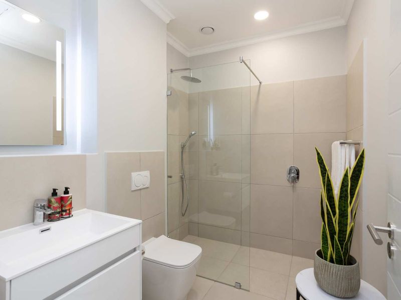 Modern bathroom featuring a walk-in shower with glass screen, wall-mounted toilet, and a sleek vanity basin with integrated lighting.