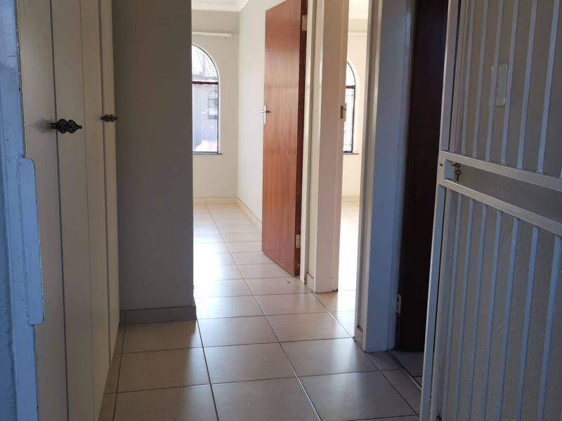 A bright, tiled hallway featuring built-in storage cupboards and a security gate, leading towards an open room with an arched window.
