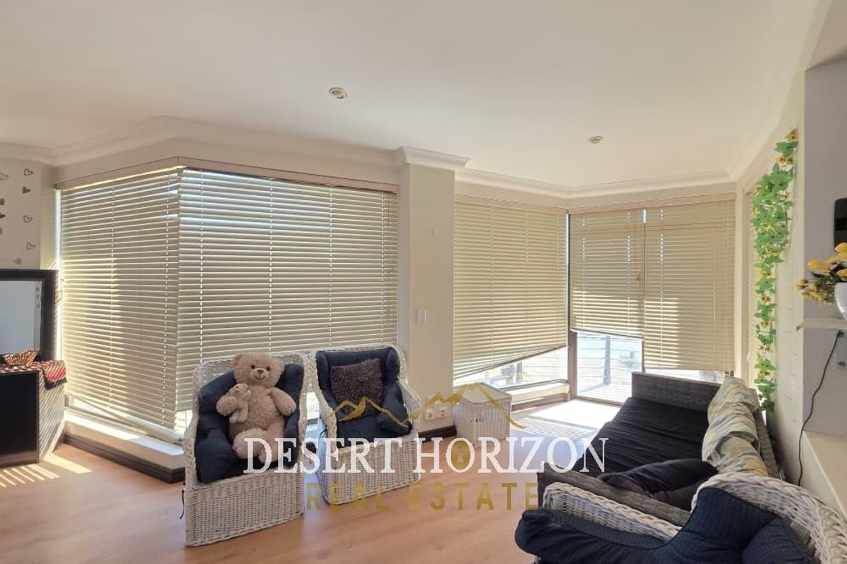 A bright living room featuring large windows with fitted venetian blinds, recessed ceiling lighting, and wood-look flooring.