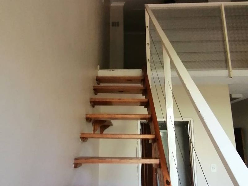 An interior view of an open-plan apartment featuring a wooden staircase leading to a mezzanine level with a metal balustrade.