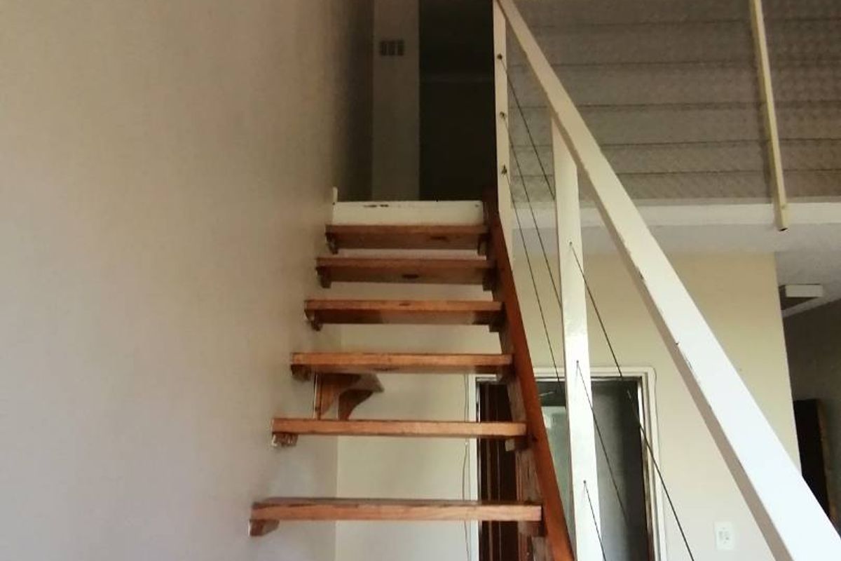 An interior view of an open-plan apartment featuring a wooden staircase leading to a mezzanine level with a metal balustrade.