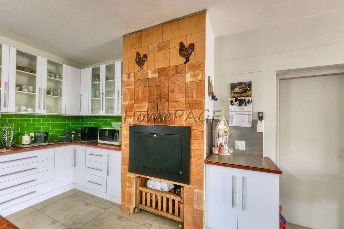 Kitchen featuring white cabinetry, green tiled splashback, and a prominent central brick fireplace feature.