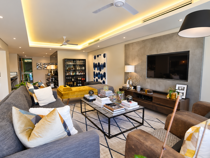 Spacious open-plan living area featuring a modern feature wall, recessed cove lighting, ceiling fans, and ducted air conditioning, seamlessly connected to the kitchen.