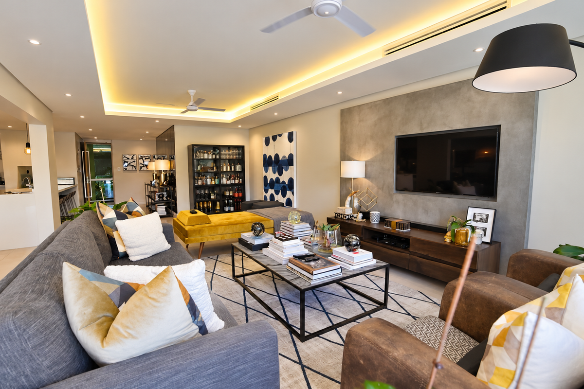 Spacious open-plan living area featuring a modern feature wall, recessed cove lighting, ceiling fans, and ducted air conditioning, seamlessly connected to the kitchen.