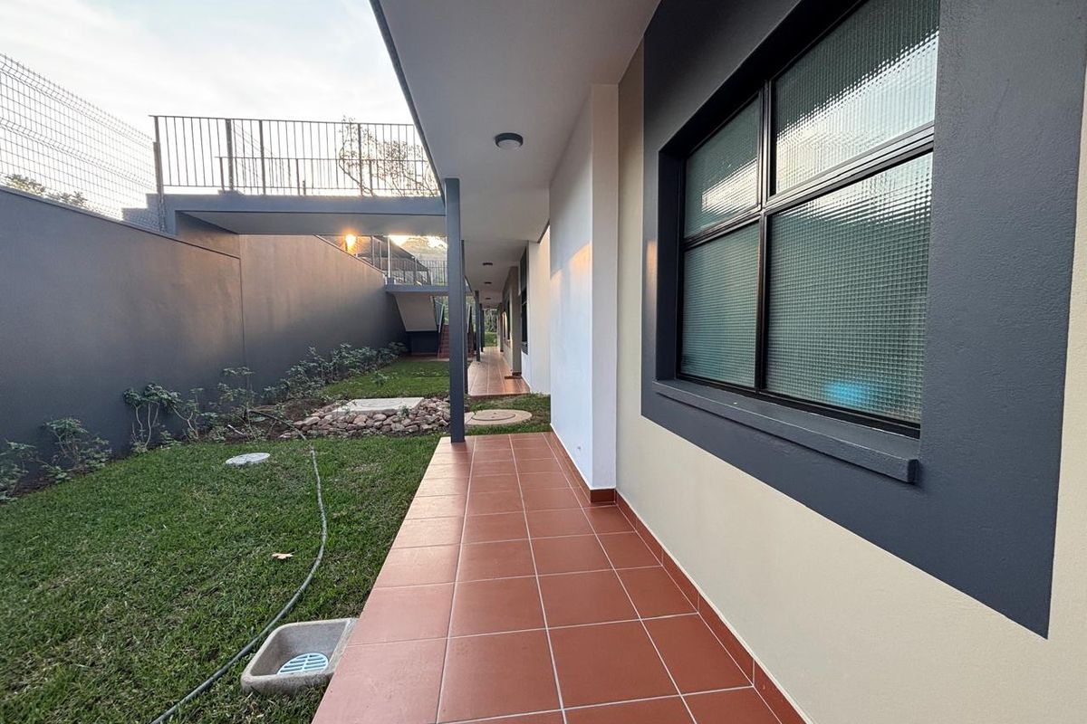 A well-maintained rear exterior area featuring a tiled patio, landscaped garden, and a metal staircase leading to an upper level.