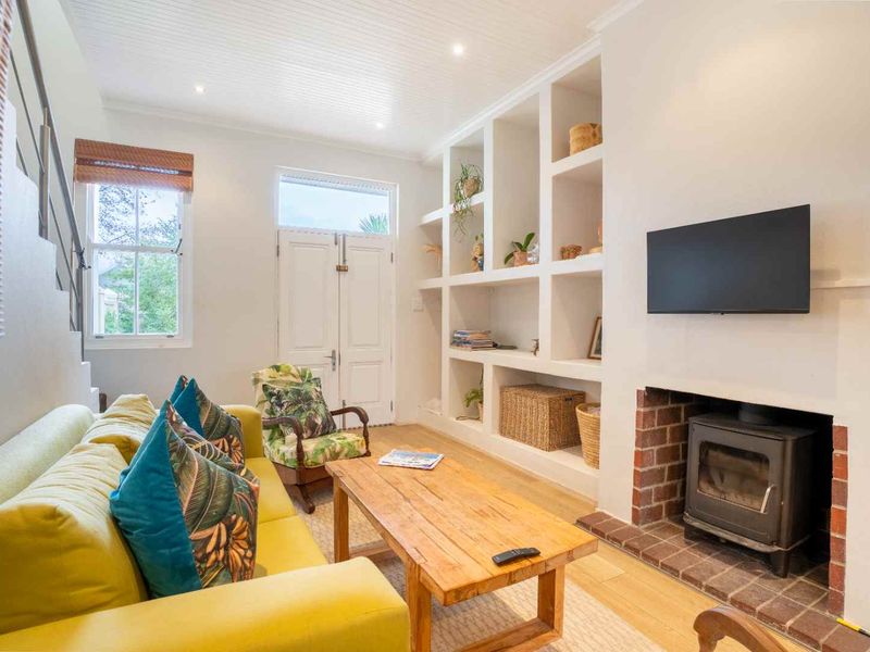 A bright living room featuring a wood-burning stove with a brick surround, built-in shelving, timber flooring, and a beadboard ceiling.