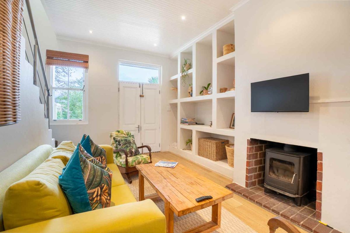 A bright living room featuring a wood-burning stove with a brick surround, built-in shelving, timber flooring, and a beadboard ceiling.
