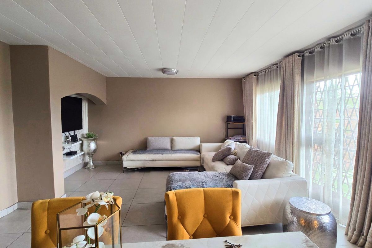 Spacious living room featuring neutral wall tones, large windows with natural light, and tiled flooring throughout.