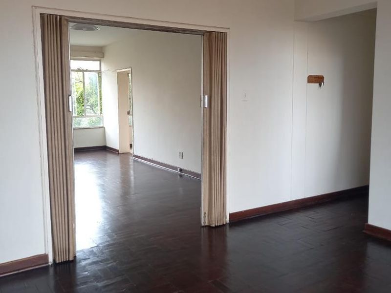 Spacious living area featuring dark parquet flooring and a folding room divider, offering a versatile layout with neutral wall finishes.