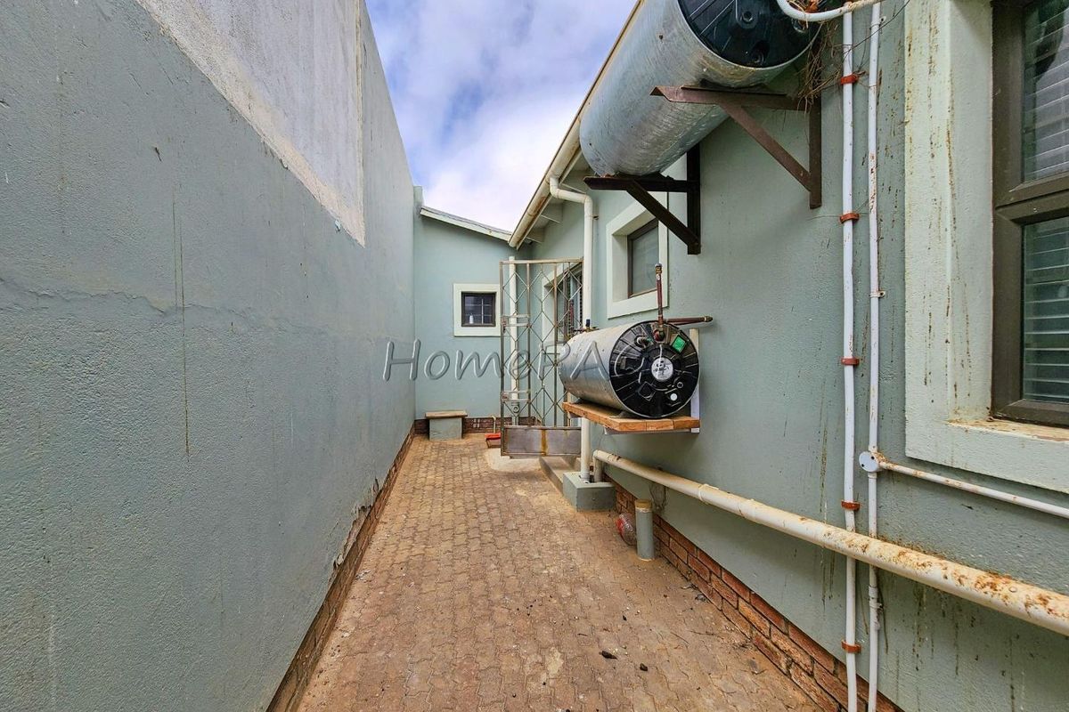 Side exterior passage featuring paved flooring, security gate, and multiple wall-mounted electric water heaters.