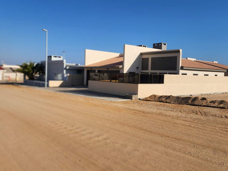 A view of the front exterior of a residential property featuring a boundary wall and tiled roof, situated along a sandy road.