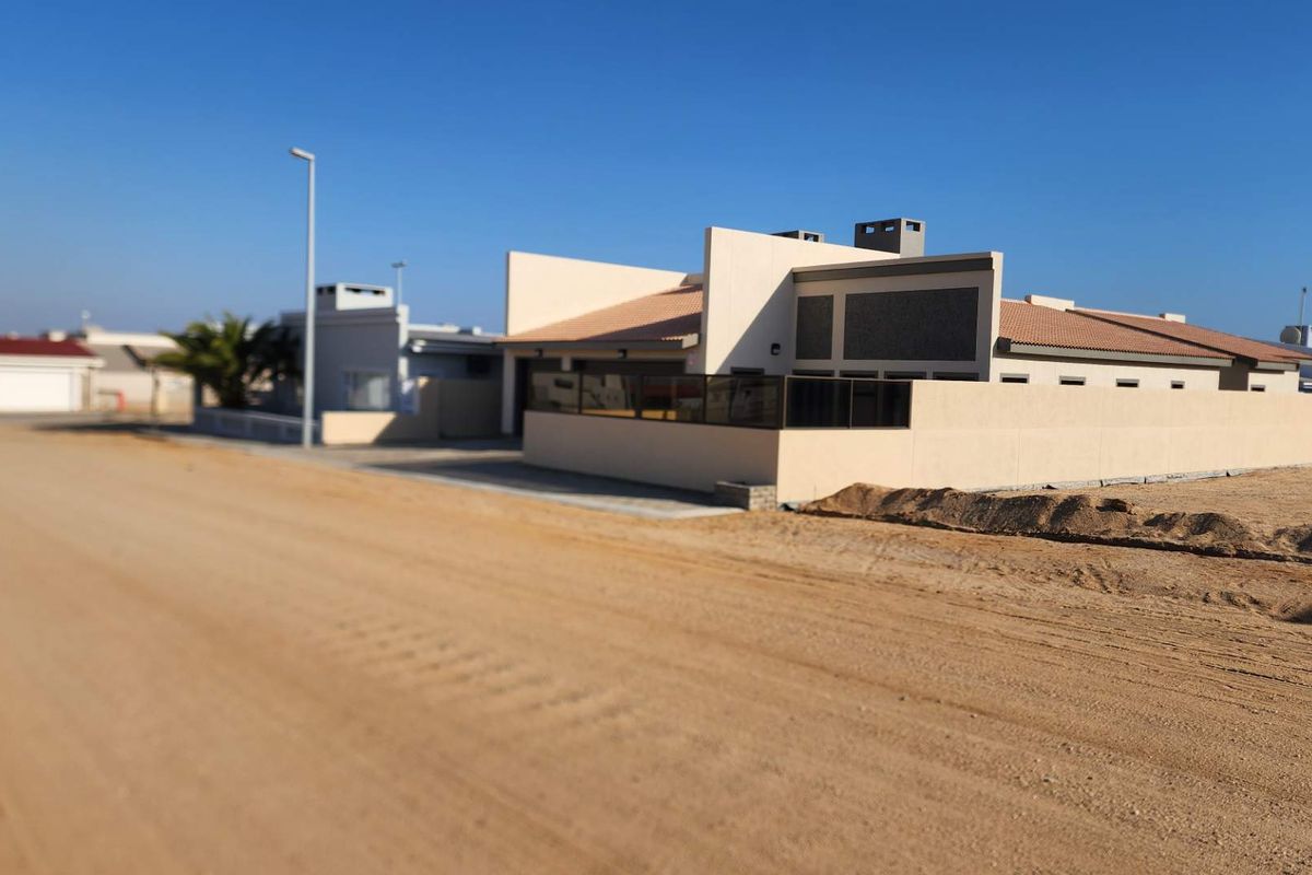 A view of the front exterior of a residential property featuring a boundary wall and tiled roof, situated along a sandy road.