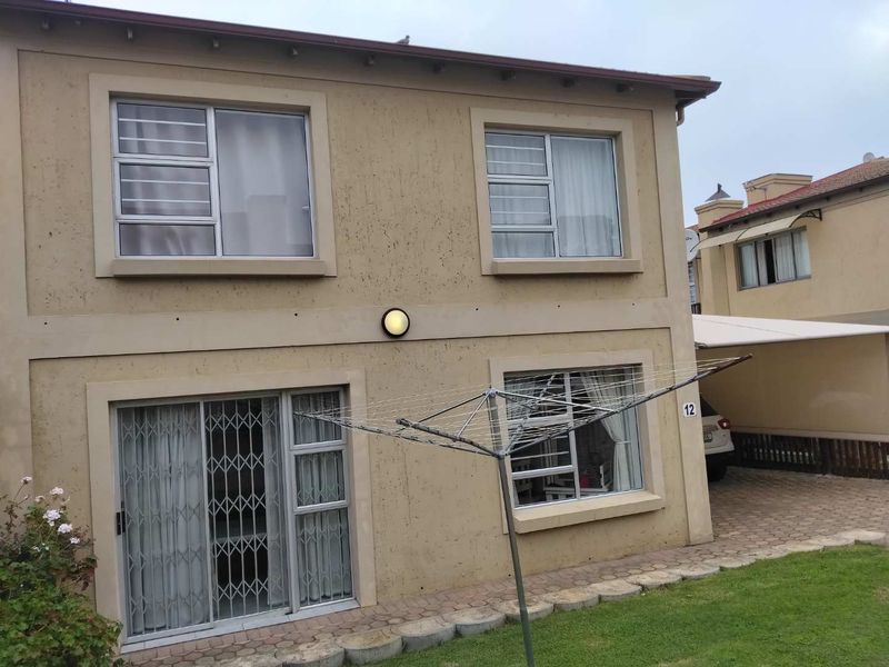 Rear view of the townhouse featuring a paved walkway, lawn, sliding glass door with security gate, and aluminium window frames.