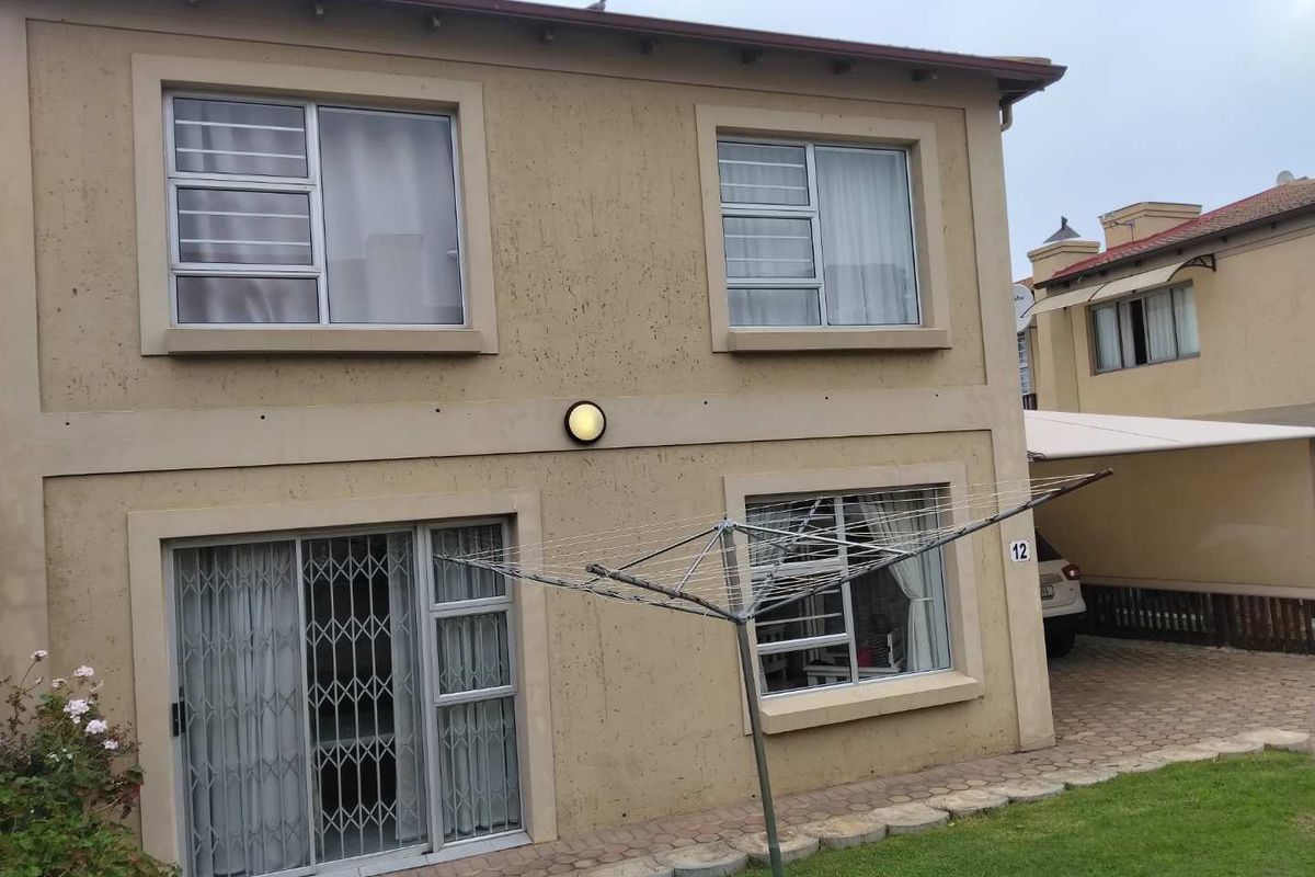 Rear view of the townhouse featuring a paved walkway, lawn, sliding glass door with security gate, and aluminium window frames.