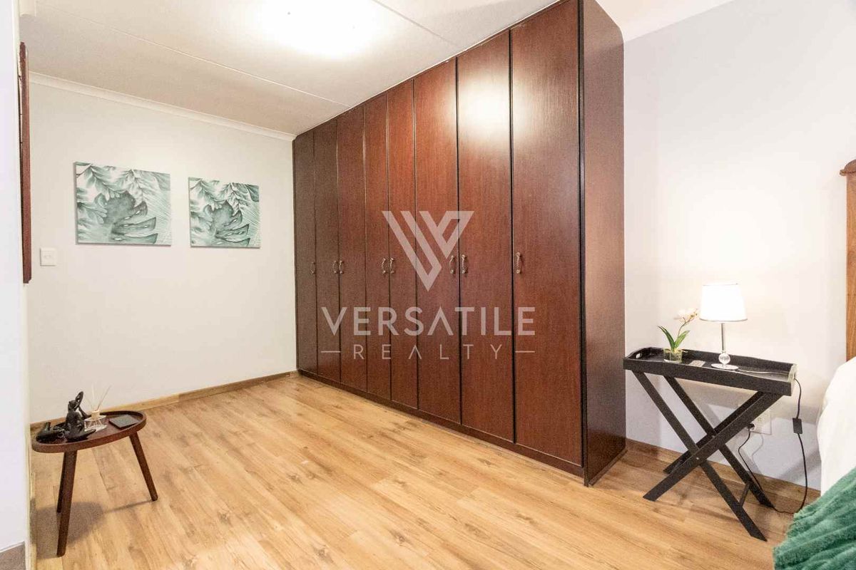 A bedroom featuring wood-look laminate flooring and a large, floor-to-ceiling built-in wooden wardrobe providing ample storage space.