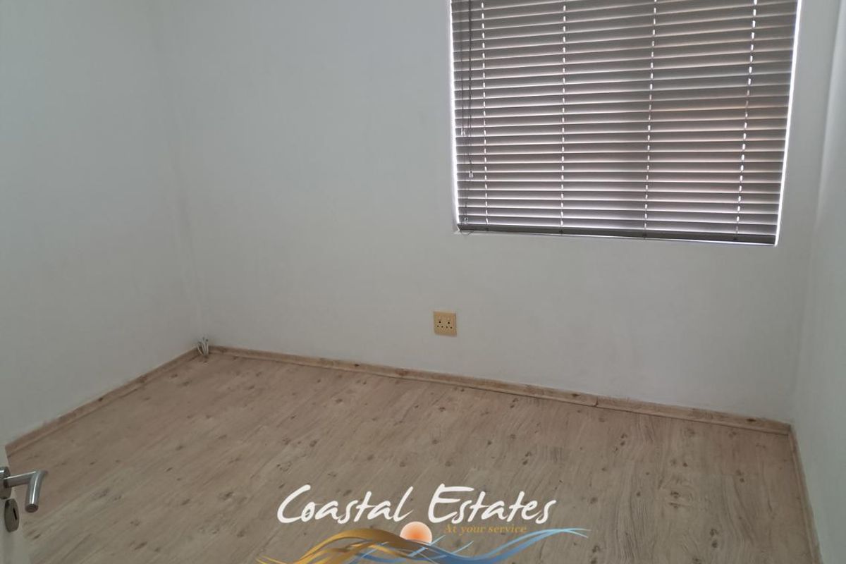 A clean, empty bedroom featuring light-toned laminate flooring, neutral walls, and fitted venetian blinds.