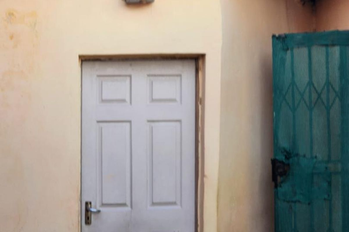 Exterior view of a side entrance featuring a panelled door and a security gate under a corrugated roof structure.