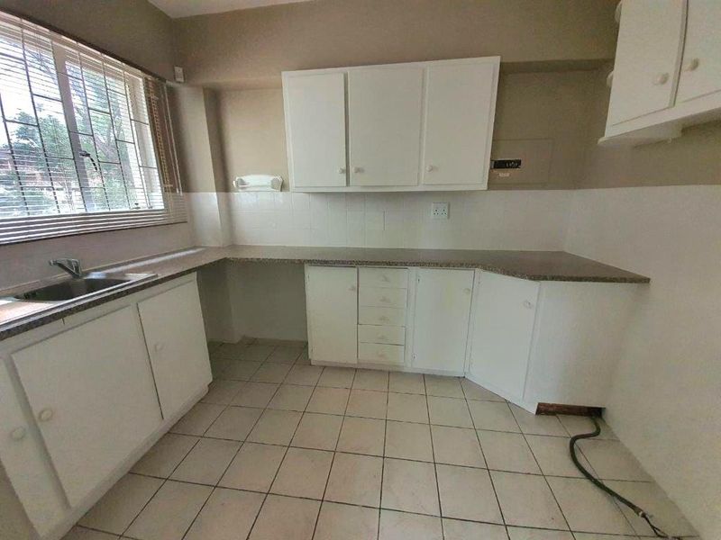 A functional, empty kitchen featuring white cabinetry, laminate countertops, a stainless steel sink, and tiled flooring, ready for a modern update.