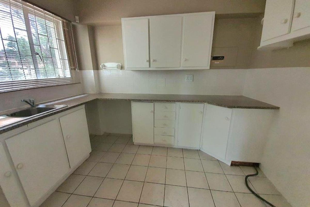 A functional, empty kitchen featuring white cabinetry, laminate countertops, a stainless steel sink, and tiled flooring, ready for a modern update.