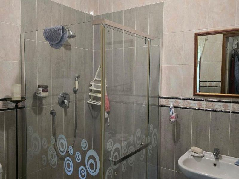 A functional bathroom featuring a glass-enclosed shower, pedestal sink, and neutral wall tiling with decorative border accents.